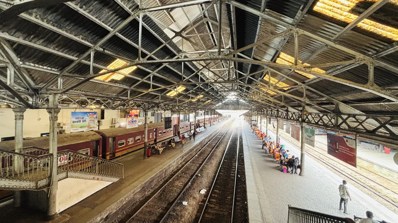 A maroon train waiting at a platform under the iron roof of Colombo Fort Station