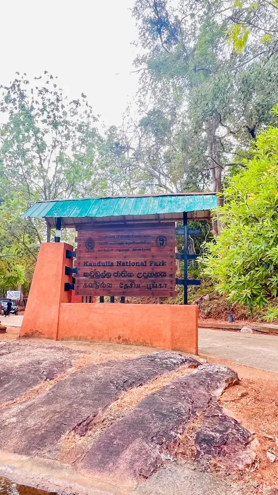 Wooden entrance sign for Kaudulla National Park under a green roof