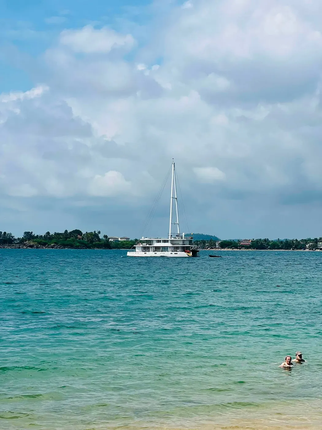Calm turquoise water at Jungle Beach with swimmers and a white boat anchored in the bay