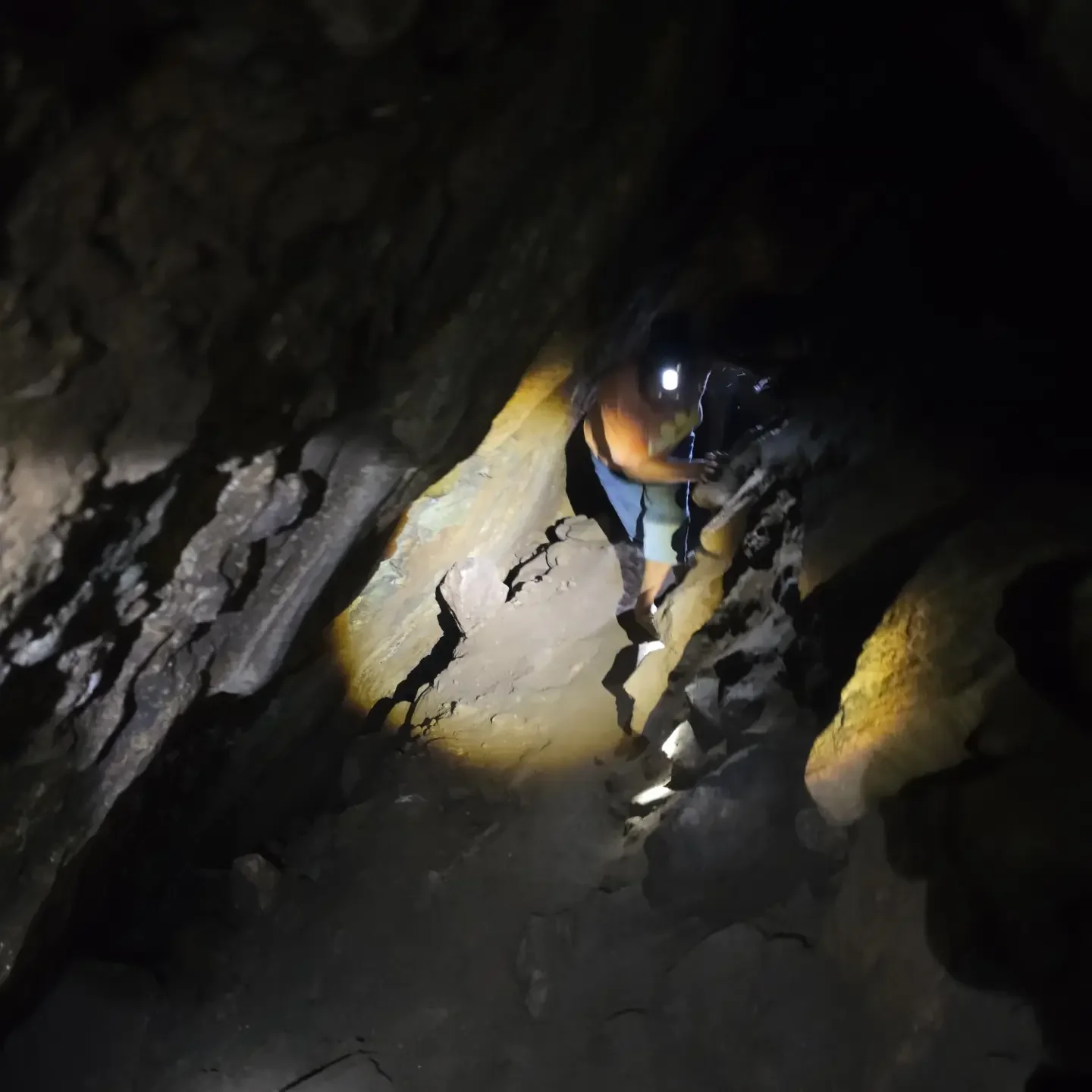 Visitor with a headlamp climbing through a narrow rocky passage in the Nil Diya Pokuna cave