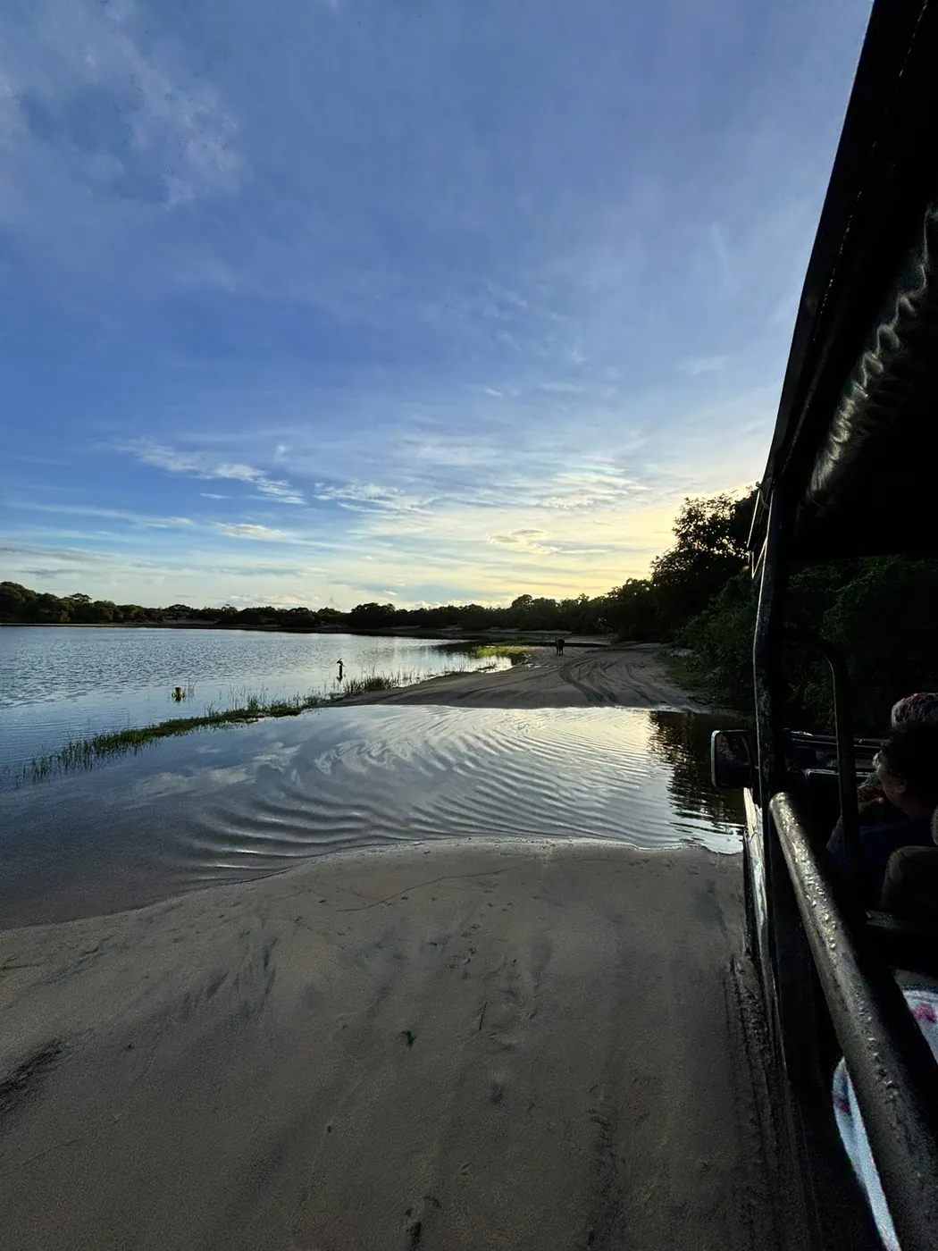 Sandbank beside a shallow villu lake at dusk with the side of a safari jeep in view